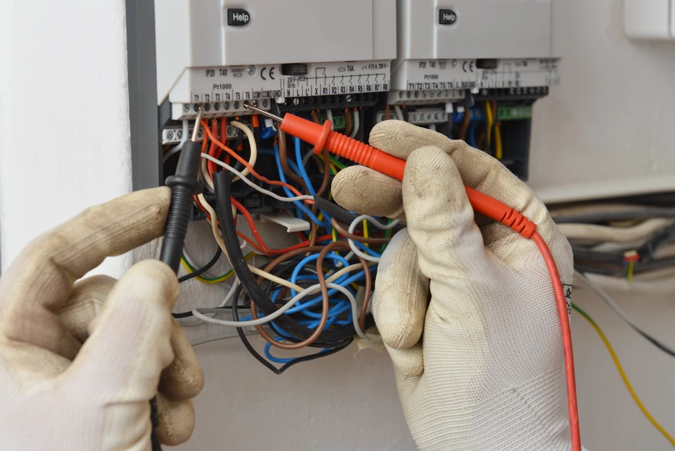 Technicien électricien portant des gants de protection travaillant sur un tableau électrique ouvert avec de nombreux câbles colorés