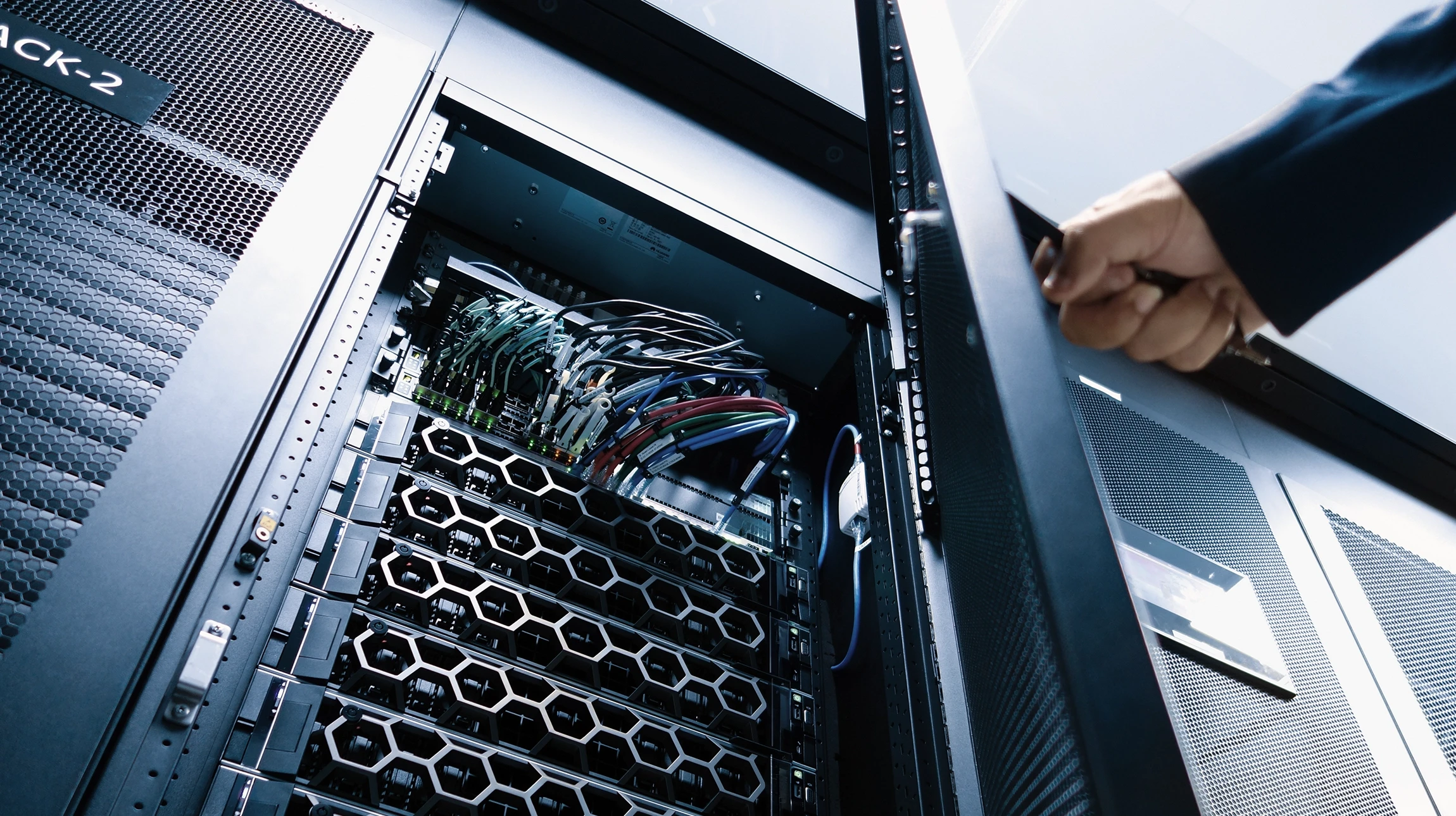 Intérieur de datacenter avec technicienne en chemise bleue utilisant une tablette tactile pour surveiller les équipements réseau